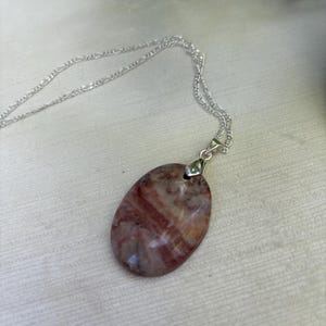 May include: A silver chain necklace with a pendant made of a red, white, and brown striped oval stone.