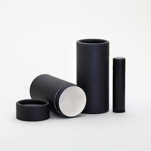 May include: Three black cardboard tubes, one with the top removed, revealing a white interior. The tubes are of different sizes, with the largest tube standing upright and the smallest tube lying on its side. The tubes are made of cardboard and have a smooth, matte finish.