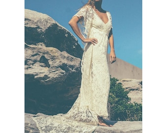 Könnte beinhalten: Ein weißes Spitzen-Hochzeitskleid mit langem Schleier und V-Ausschnitt. Das Kleid ist am Oberteil figurbetont und geht in einen weiten Rock über.