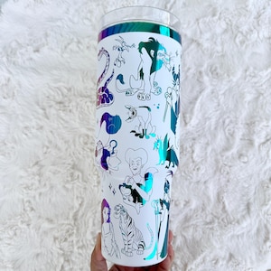 Puede incluir: Vaso blanco con tapa transparente y banda hologr&aacute;fica iridiscente. El vaso est&aacute; decorado con ilustraciones en blanco y negro de varios villanos animados. El dise&ntilde;o incluye personajes como Scar, Ursula y Cruella.
