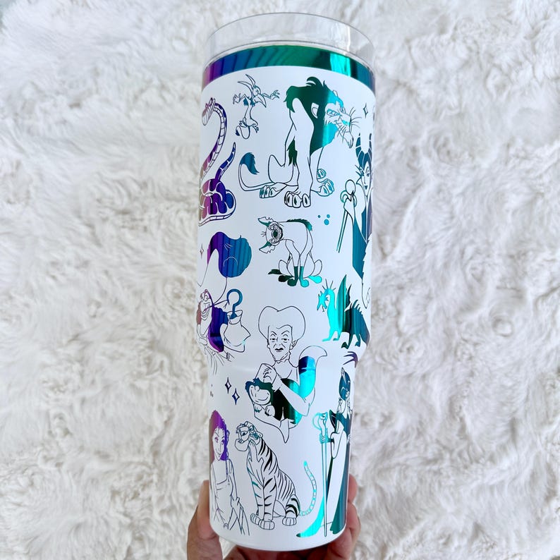 Puede incluir: Vaso blanco con tapa transparente y banda hologr&aacute;fica iridiscente. El vaso est&aacute; decorado con ilustraciones en blanco y negro de varios villanos animados. El dise&ntilde;o incluye personajes como Scar, Ursula y Cruella.