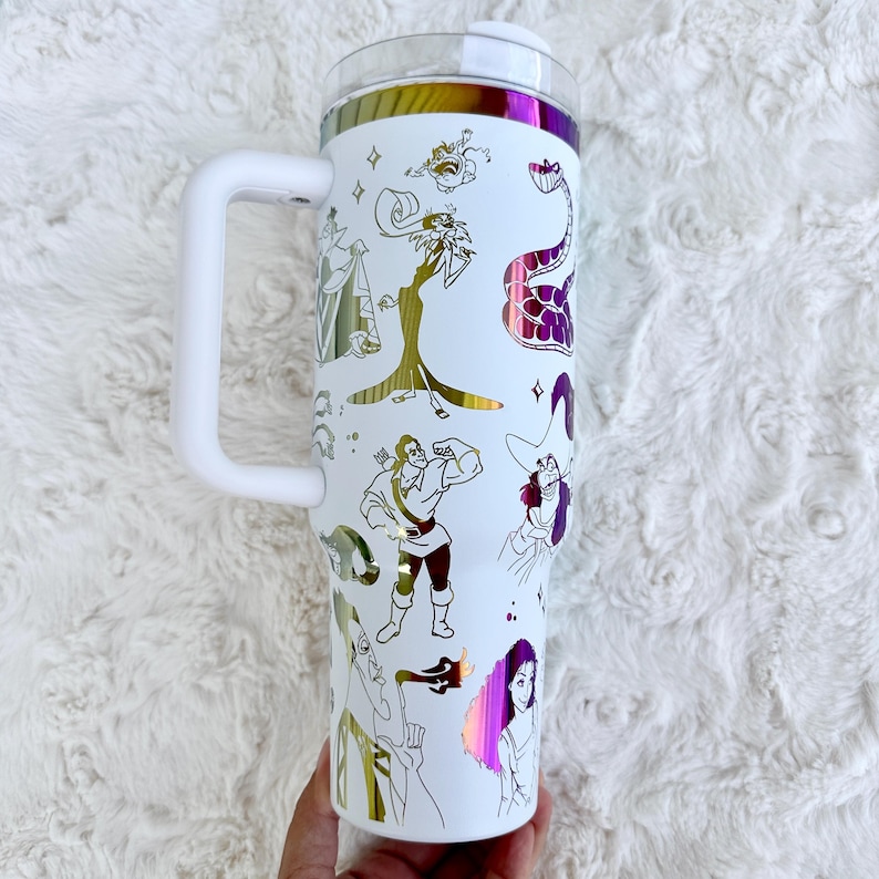 Puede incluir: Vaso t&eacute;rmico blanco con asa, con ilustraciones doradas e iridiscentes de personajes de dibujos animados. El vaso tiene una tapa transparente y un asa blanca. El dise&ntilde;o incluye varios personajes de dibujos animados. Capacidad aproximada de 887 ml.
