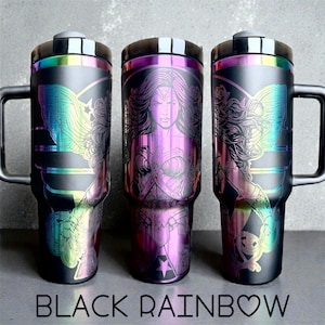 May include: Three black stainless steel travel mugs with a rainbow iridescent finish. Each mug features a graphic of Wonder Woman. The mugs have black handles and lids. The text "BLACK RAINBOW" is at the bottom.