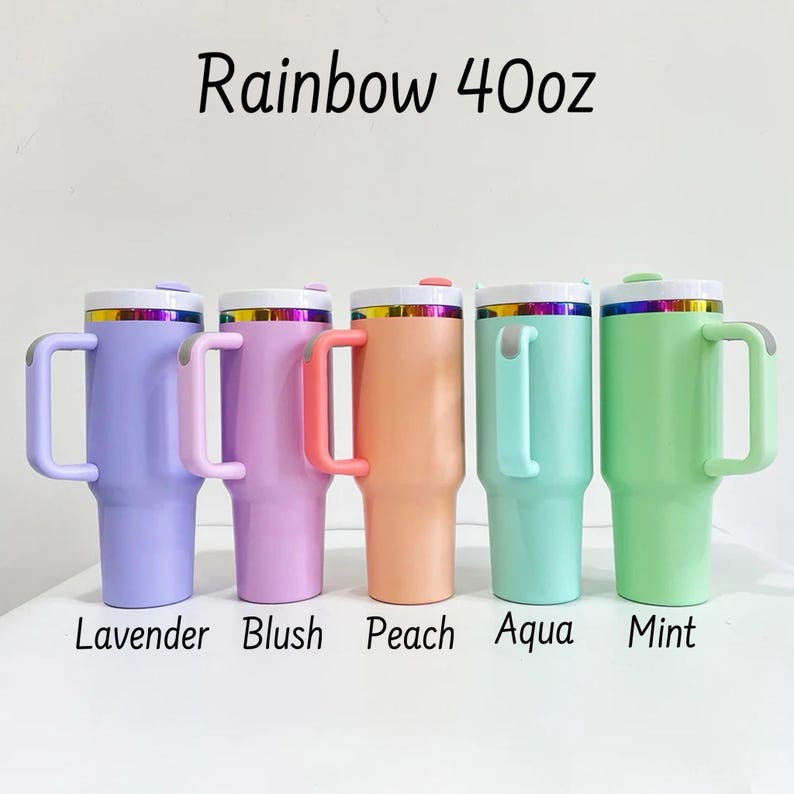 May include: Five pastel-coloured 40oz insulated tumblers are displayed, including lavender, blush, peach, aqua, and mint. Each tumbler has a white lid, a handle, and a rainbow-coloured band. The text "Rainbow 40oz" is above the tumblers.