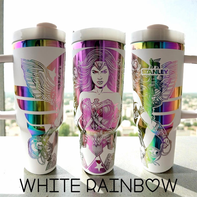 May include: Three white Stanley travel mugs with rainbow iridescent details and Wonder Woman designs. Each mug has a different design element, including the Wonder Woman logo, a portrait, and the Stanley logo. The text "WHITE RAINBOW" is at the bottom.