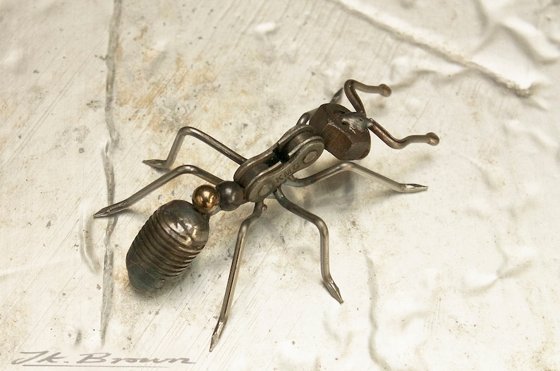 May include: A metal ant sculpture made from recycled materials, including a bike chain, nuts, and bolts. The ant is posed with its legs outstretched and its head raised.