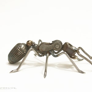 May include: A metal ant sculpture made from recycled materials, including a bicycle chain with the brand "KMC" printed on it. The ant is in a walking position with its legs extended.