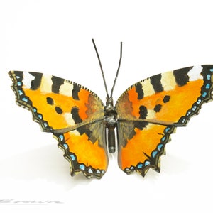 May include: A metal butterfly sculpture with orange, black, and white wings. The wings are painted to resemble a real butterfly.