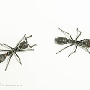 May include: Two metal ants made of screws and other metal pieces. The ants are facing opposite directions and are on a white background.