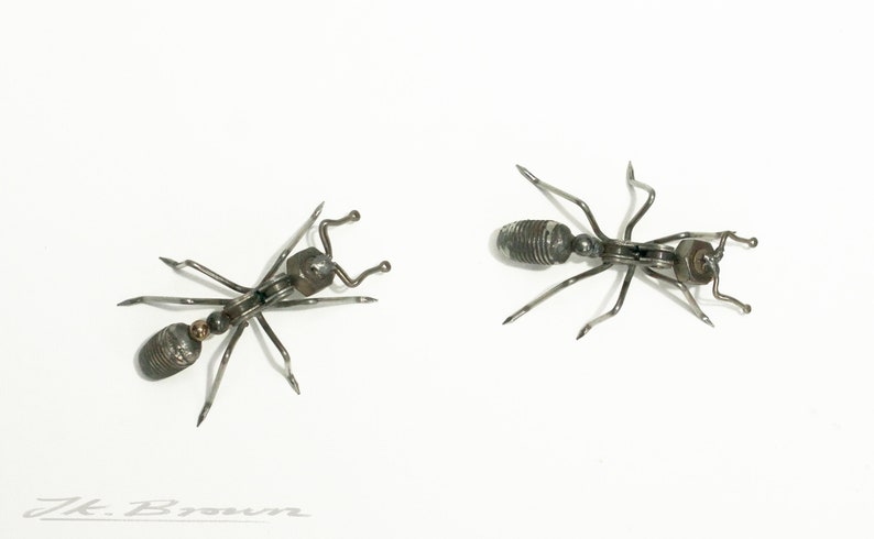 May include: Two metal ants made of screws and other metal pieces. The ants are facing opposite directions and are on a white background.