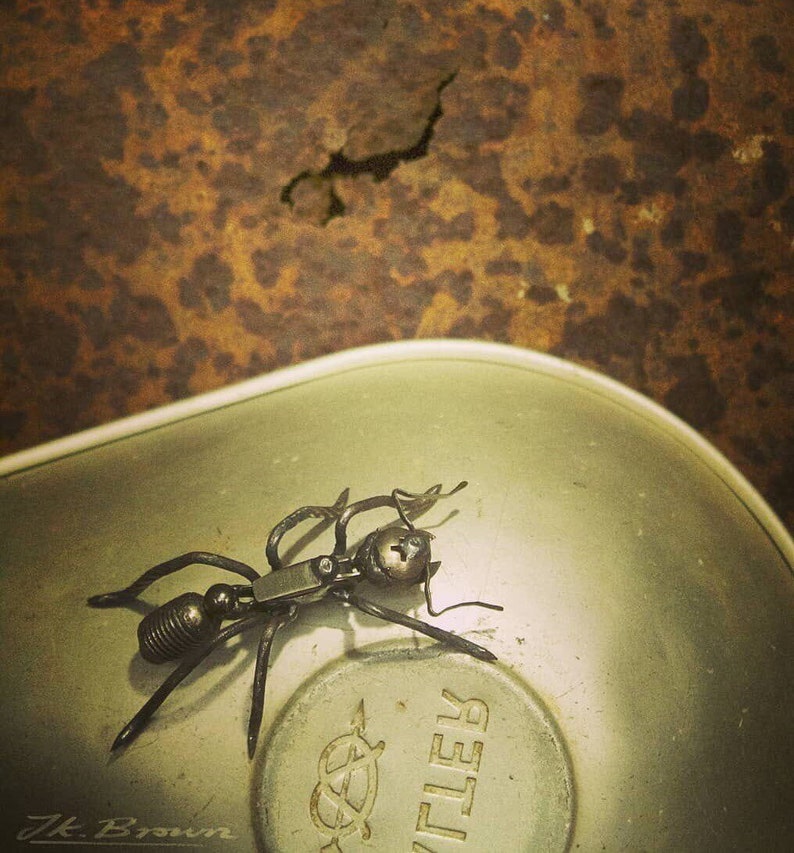 May include: A metal ant sculpture made from recycled materials. The ant is posed on a silver metal surface with the word "KTLER" printed on it.