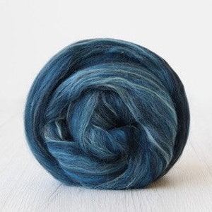May include: A ball of blue and white merino wool roving. The roving is a blend of dark blue, light blue, and white fibers.