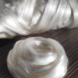 May include: A close-up of a large amount of white silk fibers. The fibers are soft and fluffy, and they are arranged in a loose, swirling pattern.
