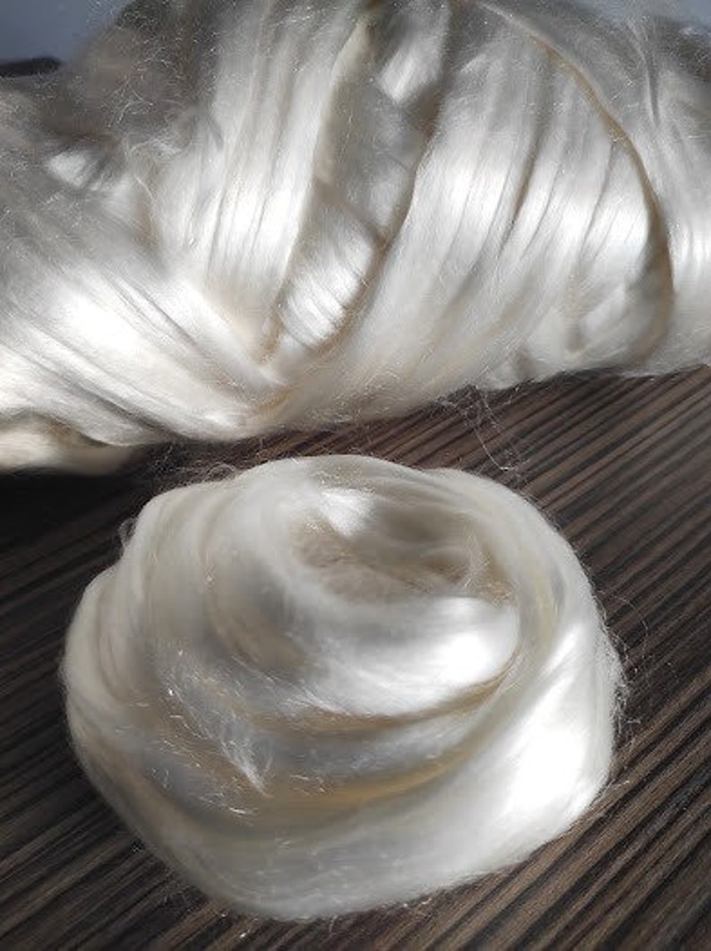 May include: A close-up of a large amount of white silk fibers. The fibers are soft and fluffy, and they are arranged in a loose, swirling pattern.