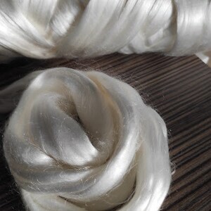 May include: A close-up of a large amount of white silk fibers. The fibers are soft and fluffy, and they are arranged in a loose, swirling pattern.