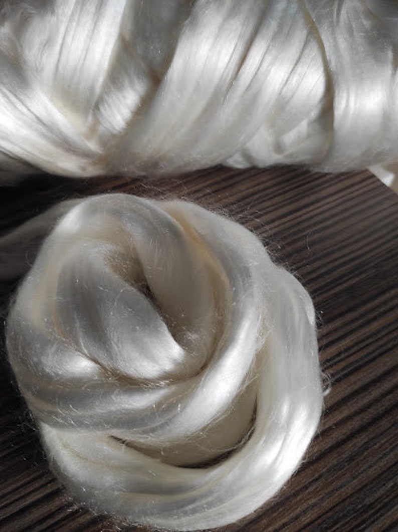 May include: A close-up of a large amount of white silk fibers. The fibers are soft and fluffy, and they are arranged in a loose, swirling pattern.