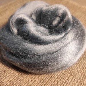 May include: A close-up of a bundle of grey and white wool roving. The roving is soft and fluffy, and it is perfect for spinning or felting.
