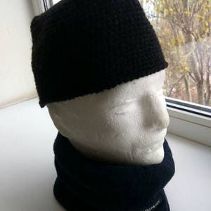 May include: A black knitted hat with a wide brim, worn on a white mannequin head. The hat is paired with a dark blue neck warmer with the word "KARRIMOR" printed on it.