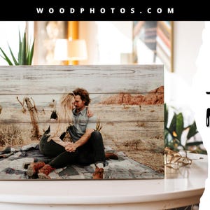 May include: A wood photo print featuring a couple embracing in a desert landscape. The print has a rustic, weathered wood background and a natural, warm color palette. The text "WOOD PHOTOS.COM" is at the top of the image and "shop NOW" is at the bottom right.
