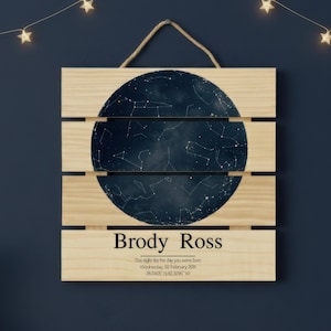 May include: Wooden sign featuring a dark blue celestial map with constellations. The sign includes the name "Brody Ross" and birth details. A rope is attached for hanging. The background is a dark blue.