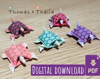 May include: Five origami paper turtles in different colors and patterns. The turtles are folded from paper and have a 3D appearance. The colors are pink, purple, blue, red, and brown. The image includes the text "Thomas & Thalia" and "DIGITAL DOWNLOAD PDF".