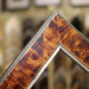 May include: Close-up of a wooden picture frame with a brown and gold finish. The frame has a beveled edge and a silver trim.