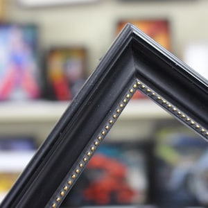 May include: Black picture frame with a gold trim. The frame has a decorative design of small gold dots along the edge.