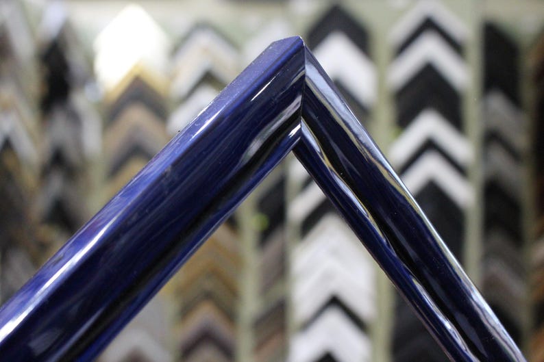 May include: A close-up of a dark blue picture frame with a glossy finish. The frame is made of wood and has a simple, elegant design.