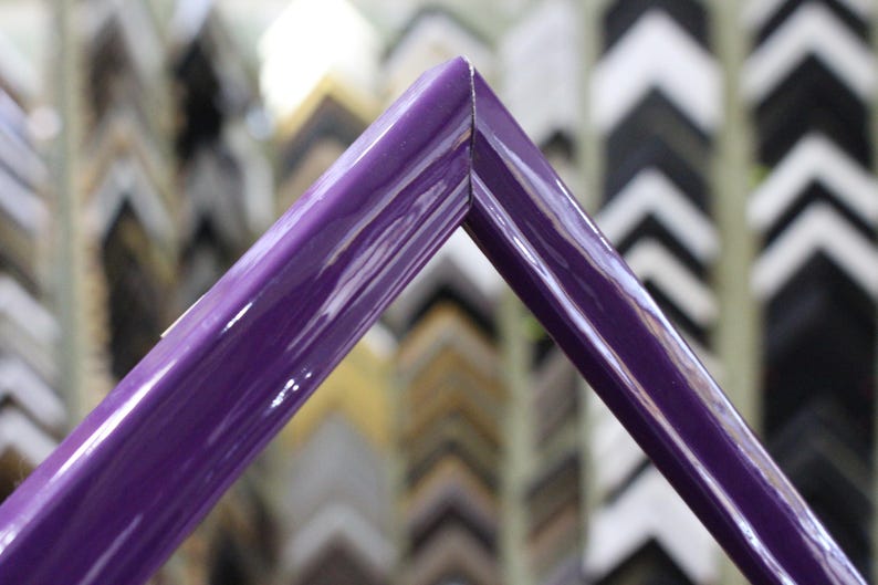 May include: Close-up of a corner of a deep purple picture frame. The frame is glossy and has a smooth finish. The frame is in focus, while the background of other frames is blurred.