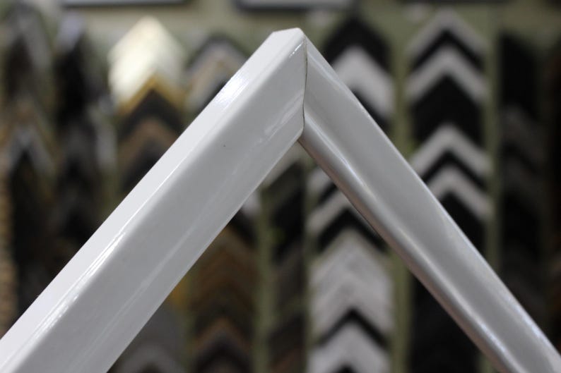 May include: Close-up of a white picture frame with a smooth, glossy finish. The frame is made of a sturdy material and has a simple, modern design.