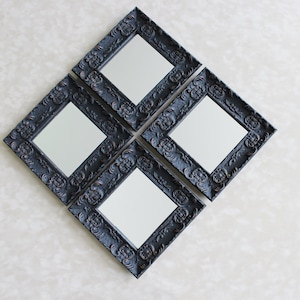 May include: Four black framed mirrors with ornate detailing arranged in a diamond shape on a white wall.