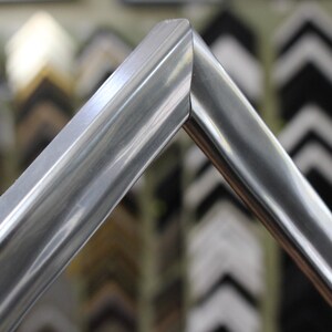 May include: Close-up of a silver picture frame with a beveled edge. The frame is made of metal and has a polished finish.