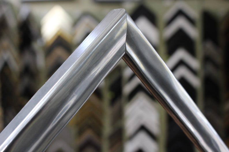 May include: Close-up of a silver picture frame with a beveled edge. The frame is made of metal and has a polished finish.