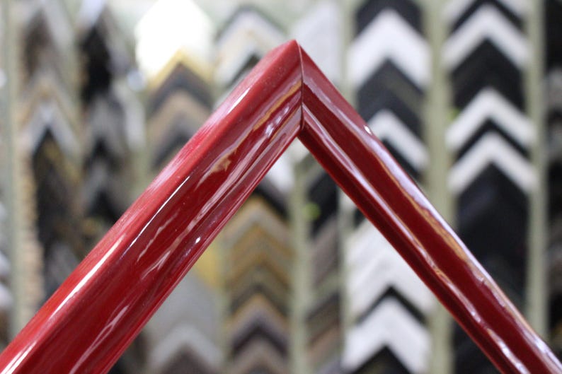 May include: A close-up of a red picture frame with a glossy finish. The frame is made of wood and has a simple, elegant design.
