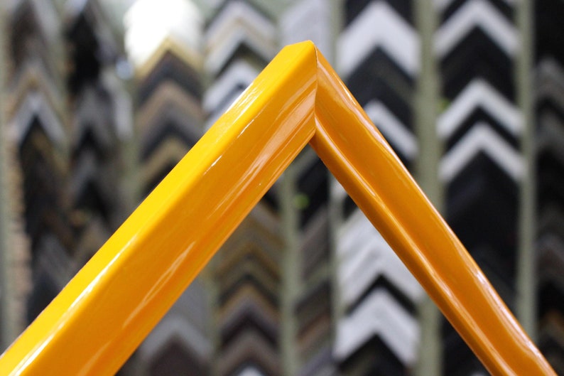 May include: A close-up of a bright yellow picture frame. The frame is made of wood and has a smooth, glossy finish.
