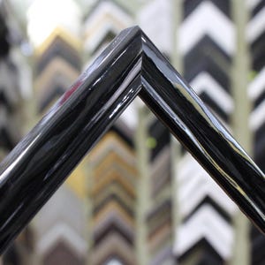 May include: Close-up of a black picture frame with a smooth, glossy finish. The frame is angled to show the corner detail.