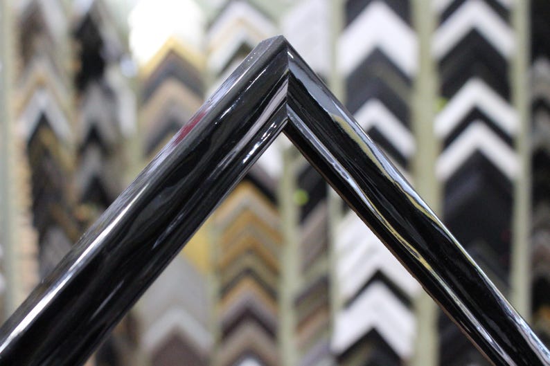 May include: Close-up of a black picture frame with a smooth, glossy finish. The frame is angled to show the corner detail.