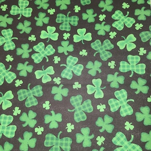 May include: Black fabric with a repeating pattern of green shamrocks. Some of the shamrocks have a checkered pattern.