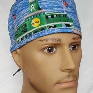 Può includere: Un berretto chirurgico blu e verde con un design a forma di traghetto. Il berretto ha una cravatta sul retro e le parole "Ferry" sulla barca.