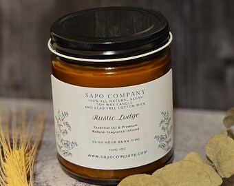 May include: A brown glass candle jar with a black lid. The label reads "SAPO COMPANY 100% ALL NATURAL VEGAN SOY WAX CANDLE AND LEAD FREE COTTON WICK Rustic Lodge Essential Oil & Premium Natural Fragrance Infused 55-60 HOUR BURN TIME 150G-70Z www.sapocompany.com".