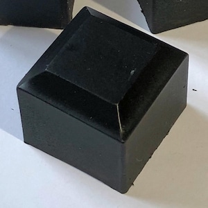 Puede incluir: Una pastilla de jabón negra de forma cuadrada.