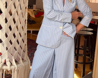 Puede incluir: Un conjunto de pijama a rayas azul claro con ribete blanco, que consta de una blazer y unos pantalones capri. El atuendo se combina con tacones beige de punta con hebilla. La persona lleva gafas de sol y medias blancas.