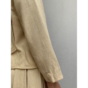 Puede incluir: Una chaqueta de lino beige con un solo bot&oacute;n en la manga.