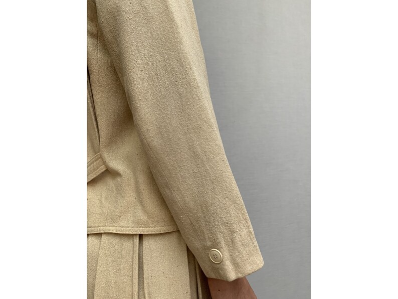 Puede incluir: Una chaqueta de lino beige con un solo bot&oacute;n en la manga.