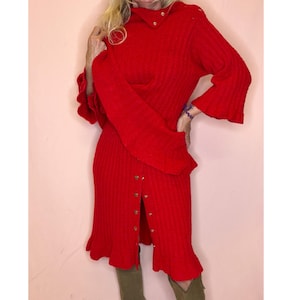 Peut inclure: Une robe en tricot côtelé rouge vif dotée d'un col montant avec des boutons dorés, de manches longues à poignets volantés et d'une fermeture boutonnée sur le devant jusqu'à l'ourlet. La robe présente un corsage ajusté et une jupe évasée.