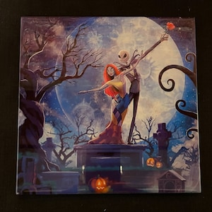Peut inclure: Une illustration colorée de Jack Skellington et Sally de L'Étrange Noël de monsieur Jack dansant devant une pleine lune. L'arrière-plan présente un cimetière avec des arbres fantasmagoriques et des citrouilles.