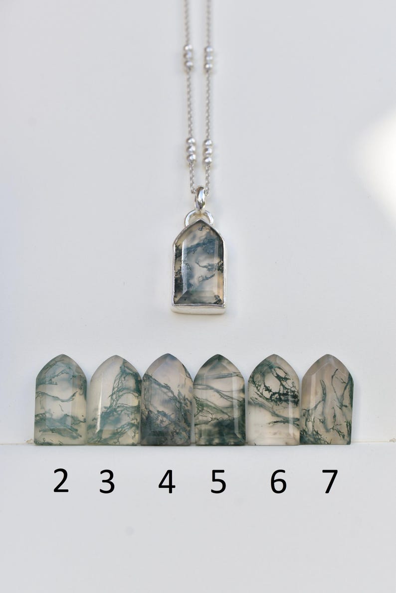 May include: A silver necklace with a pointed arch pendant containing a moss agate stone with green inclusions. Below are six loose, matching moss agate stones in the same pointed arch shape, labeled with the numbers 2, 3, 4, 5, 6, and 7.