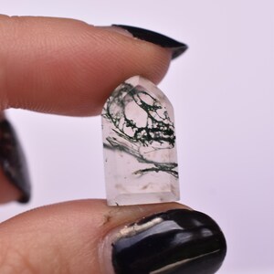 May include: A small, polished, clear quartz crystal tower with a pointed top and a flat base. The stone features distinct, dark green, moss-like dendritic inclusions that branch throughout the transparent interior of the mineral specimen.