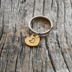 May include: A silver key chain with a gold heart charm. The heart charm has a smaller heart cut out in the center.