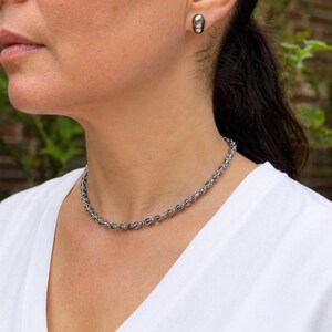 Peut inclure: Un collier en argent avec de petites perles colorées et des boucles d'oreilles assorties. Le collier est composé d'une chaîne délicate avec des perles bleues, vertes et roses alternées. Les boucles d'oreilles sont des clous d'oreilles gris foncé de forme ovale.